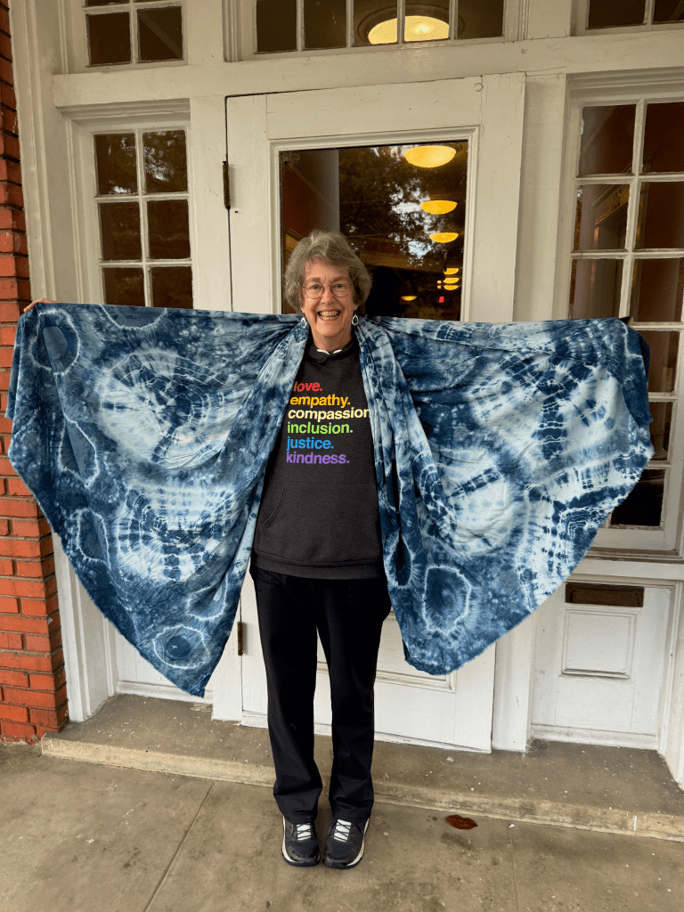 Photo of customer with indigo dyed shawl giving herself wings. Front porch of historic Mercy Hospital building where I was born.
